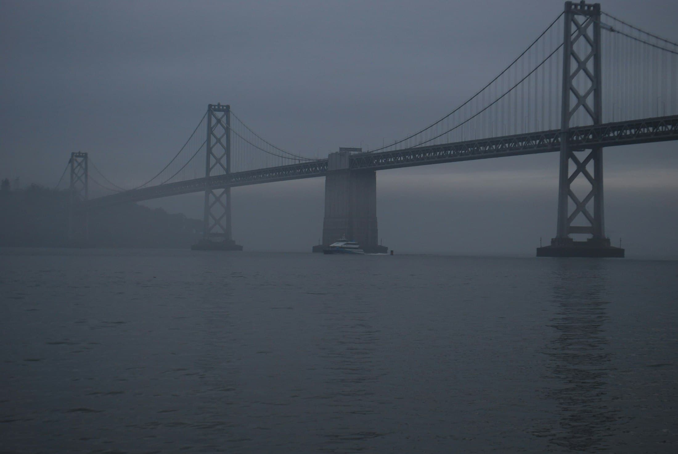 The Bay Bridge fading into fog over still water